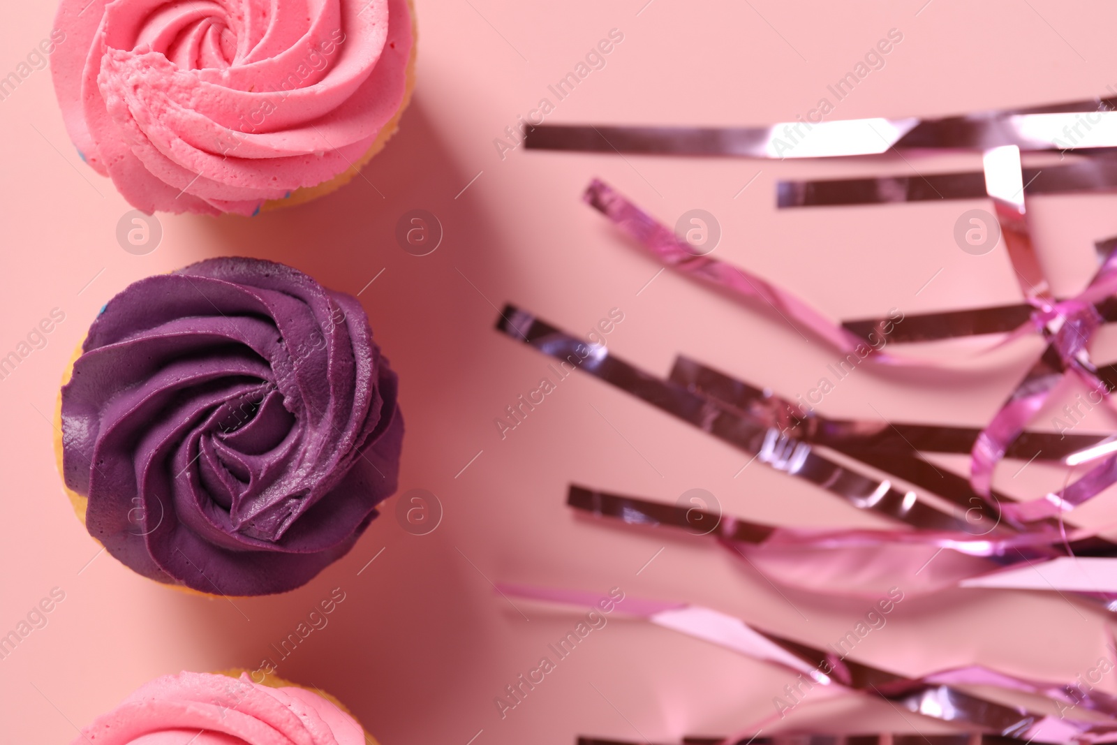 Photo of Delicious cupcakes with bright cream and confetti on pink background, flat lay