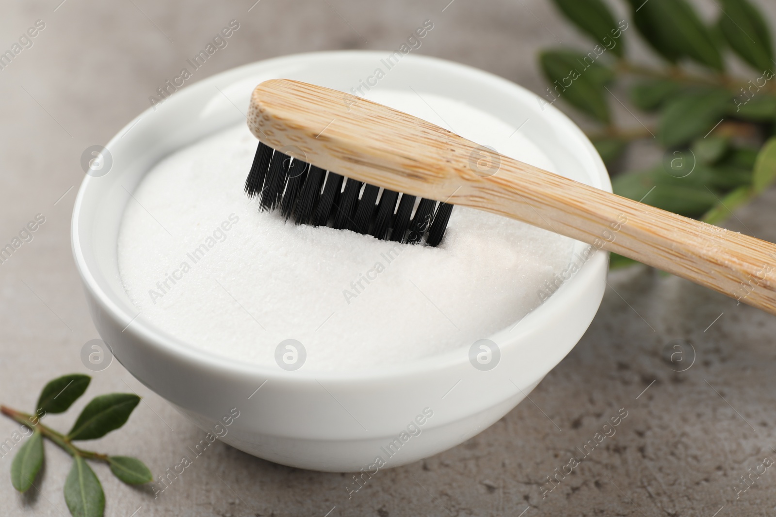 Photo of Bamboo toothbrush and bowl of baking soda on grey table, closeup