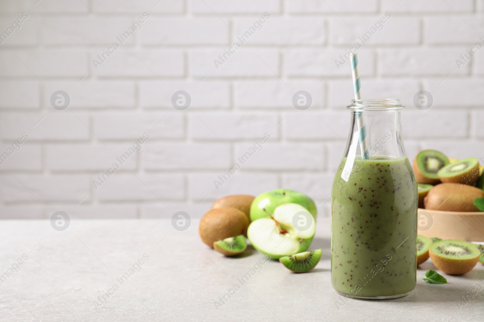 Photo of Delicious kiwi smoothie and fresh fruits on light table. Space for text