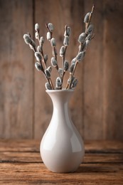 Photo of Beautiful bouquet of pussy willow branches in vase on wooden table