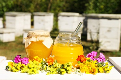 Photo of Delicious fresh honey and beautiful flowers on white wooden table in garden
