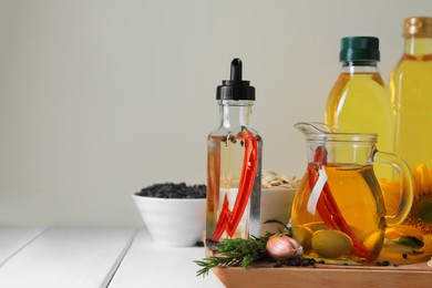 Different cooking oils and ingredients on white wooden table against light background, space for text