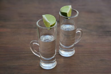 Photo of Mexican tequila shots with lime slices on wooden table