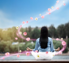 Woman meditating near river, back view. Flowers flying around her symbolizing state of mindfulness