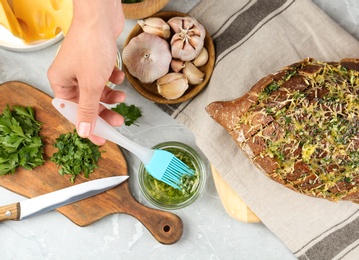 Photo of Woman brushing tasty homemade bread with garlic and herbs at light table, top view