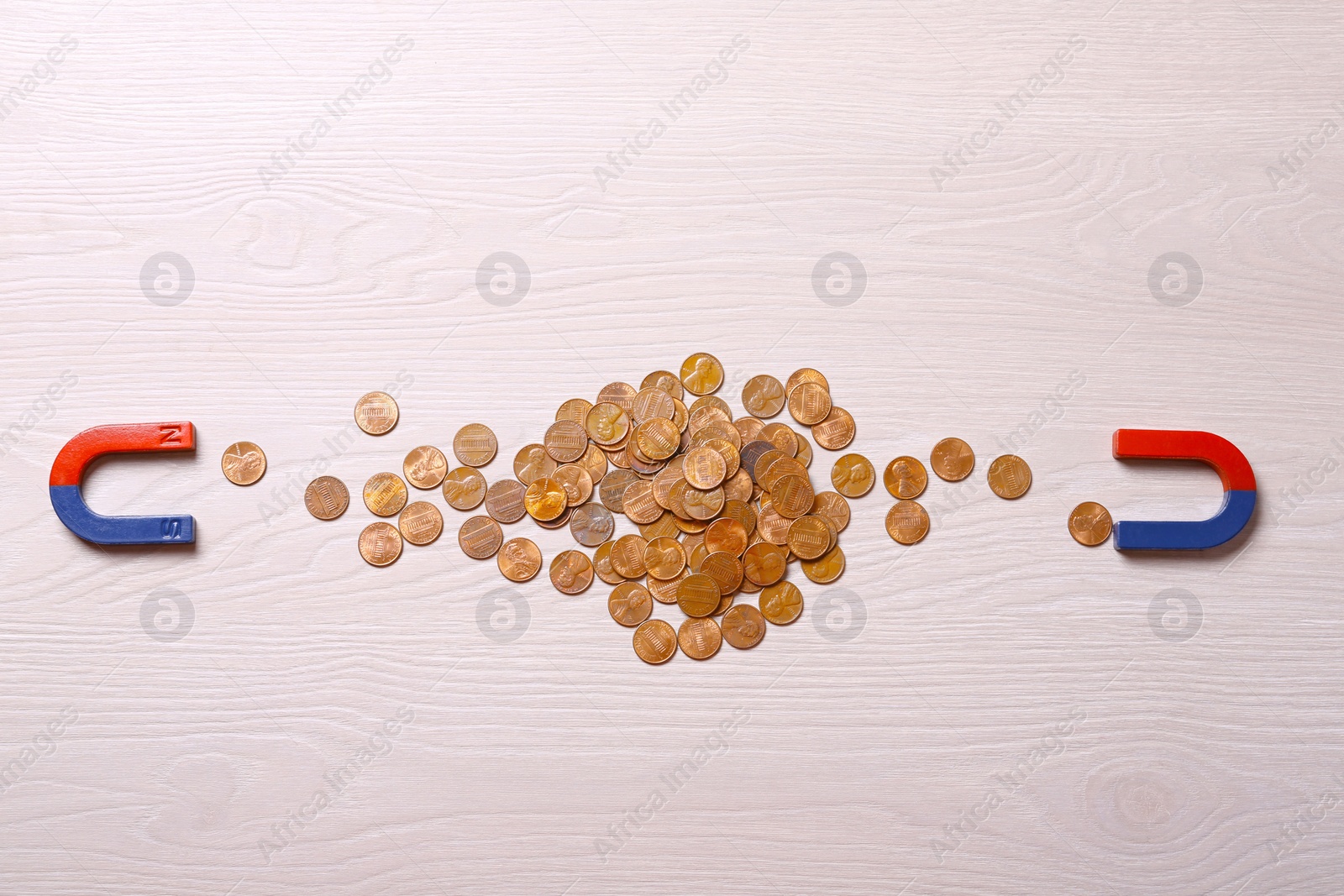 Photo of Magnets attracting coins on light wooden background, flat lay