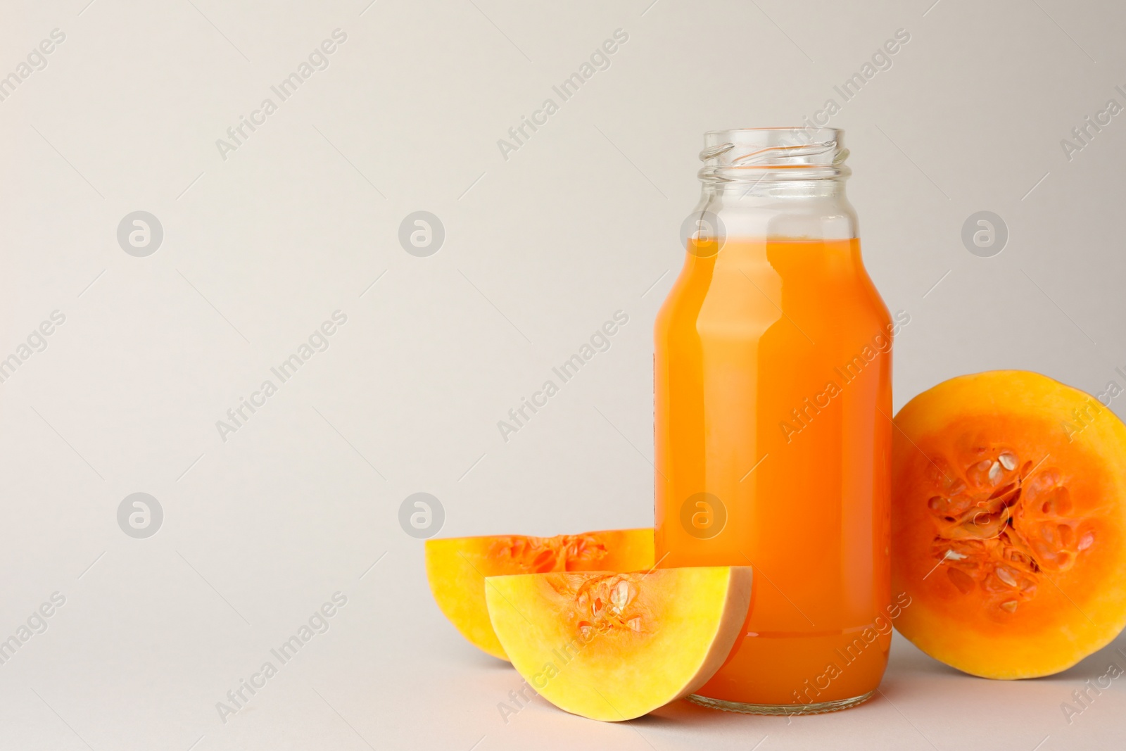 Photo of Tasty pumpkin juice in glass bottle and cut pumpkin on light background. Space for text