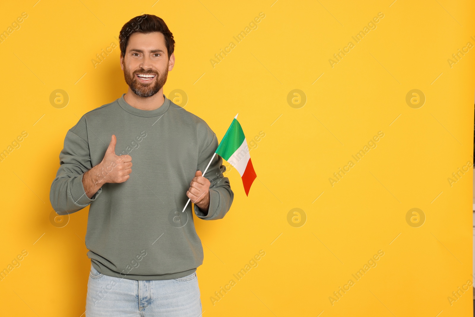 Photo of Man with flag of Italy showing thumb up on yellow background, space for text