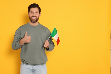 Photo of Man with flag of Italy showing thumb up on yellow background, space for text