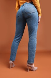 Woman in stylish jeans on brown background, closeup