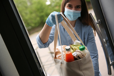 Photo of Female volunteer giving bag with products through doorway, closeup. Aid during coronavirus quarantine