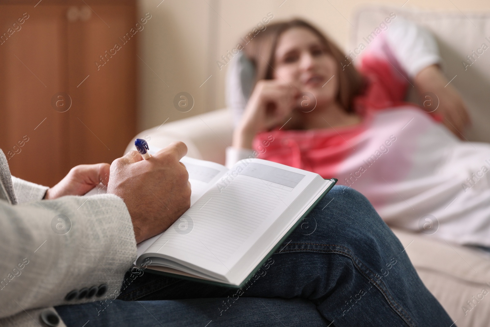 Photo of Professional psychotherapist and patient in office, focus on hands with notebook