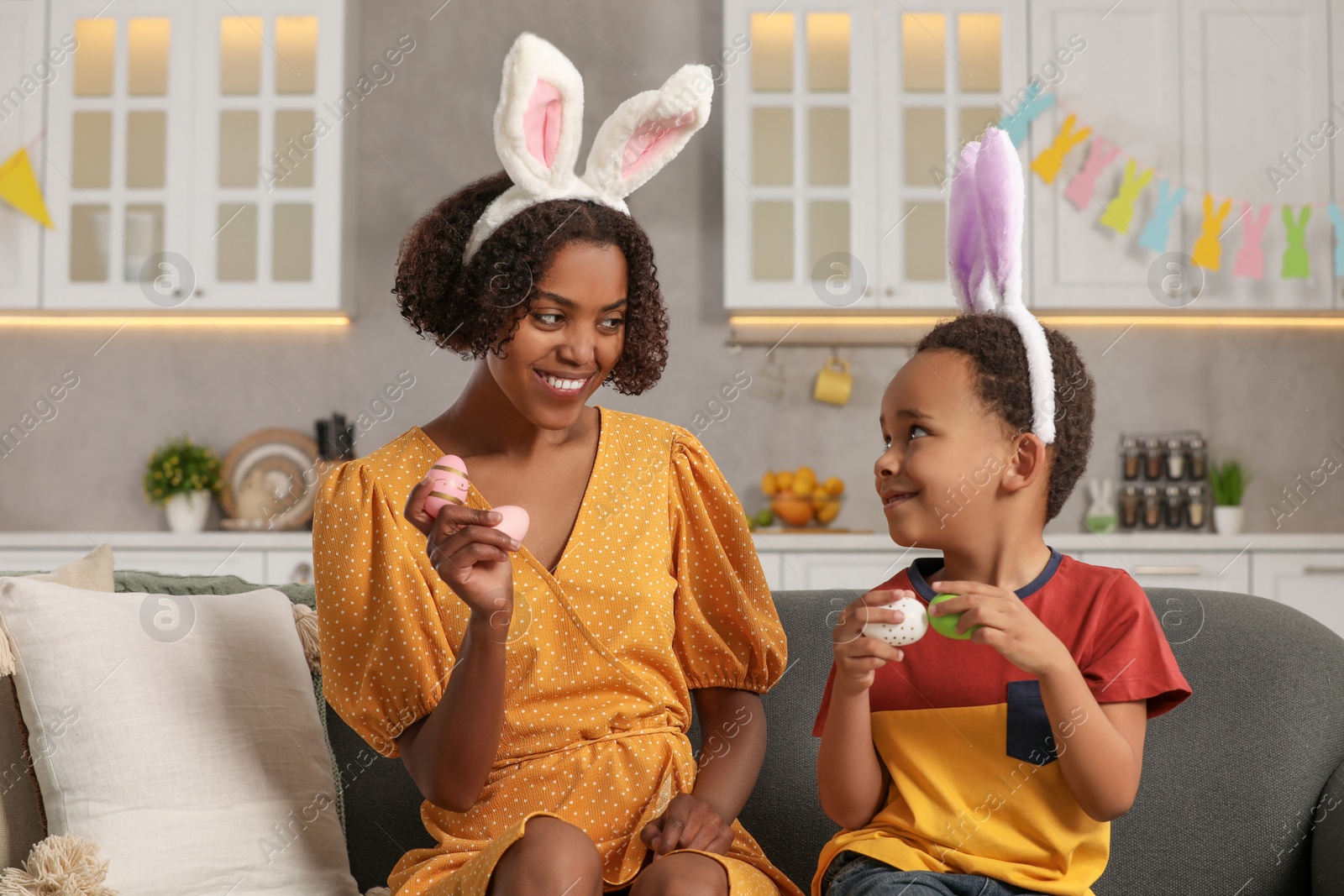 Photo of Happy African American mother and her cute son with Easter eggs in kitchen