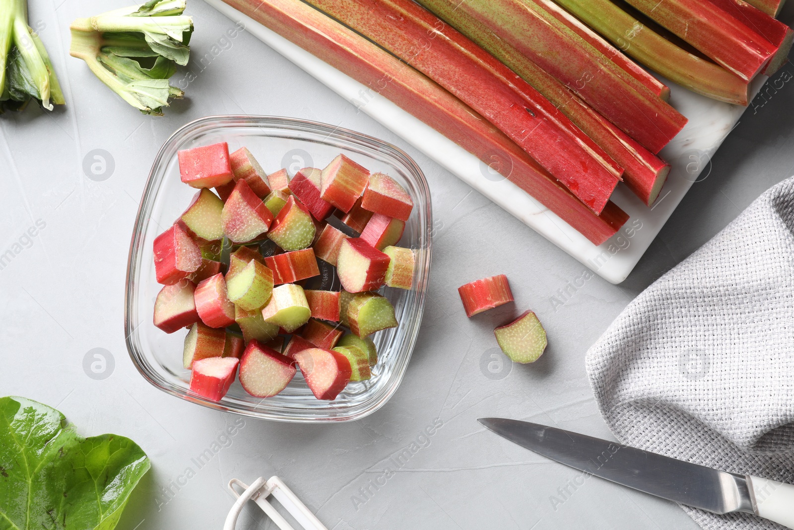 Photo of Whole and cut rhubarb stalks and knife on white table, flat lay