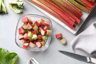 Whole and cut rhubarb stalks and knife on white table, flat lay