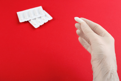 Photo of Woman holding suppository on red background, closeup. Hemorrhoid treatment