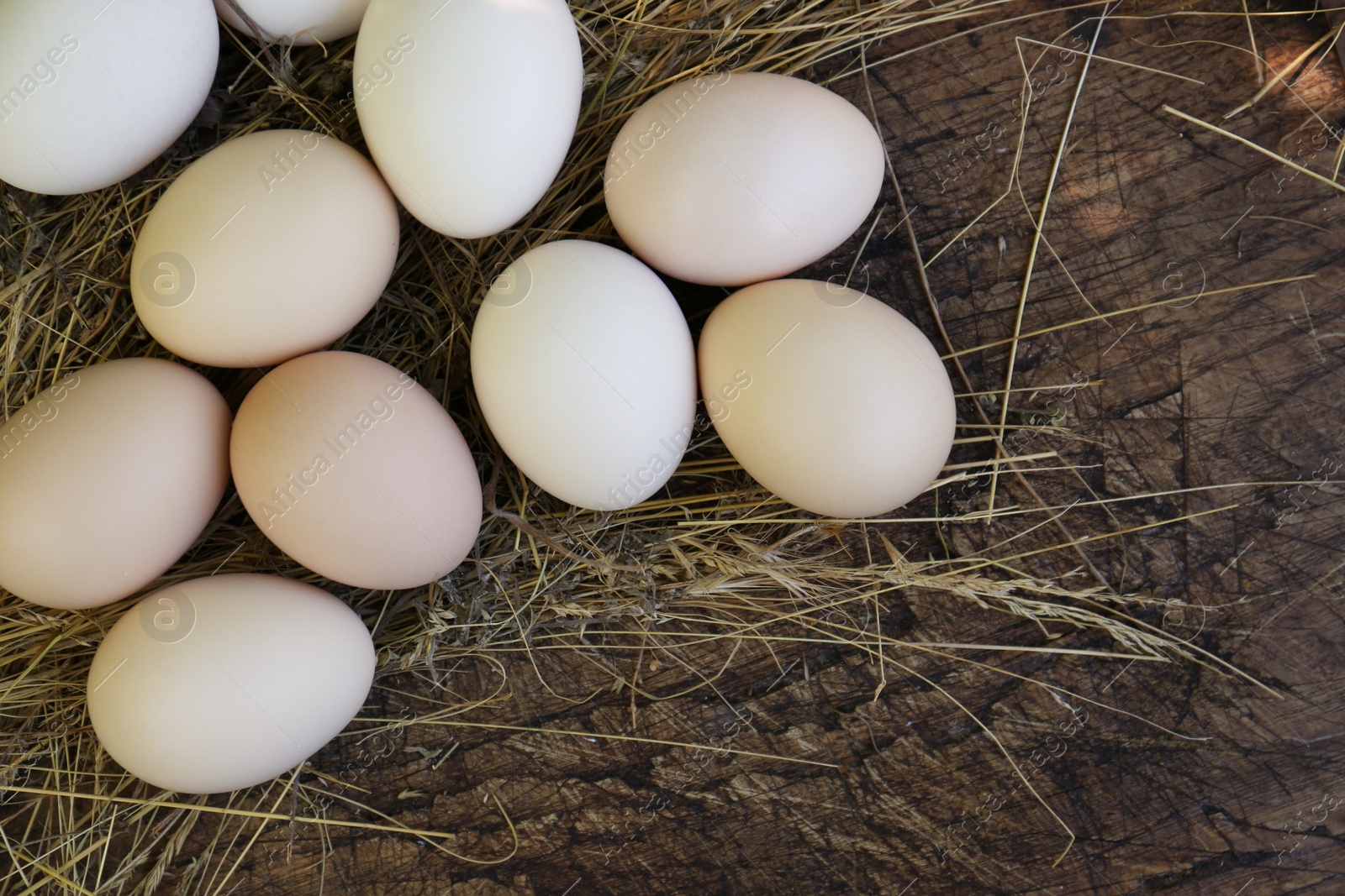 Photo of Fresh raw eggs and straw on wooden surface, flat lay