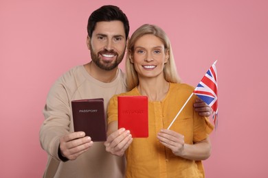 Immigration. Happy couple with passports and flag of United Kingdom on pink background