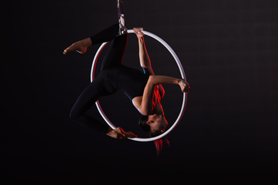 Photo of Young woman performing acrobatic element on aerial ring against dark background