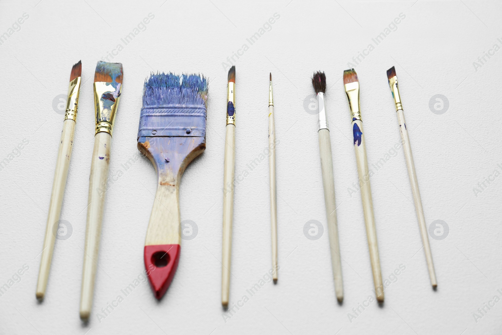 Photo of Different brushes with colorful paints on white canvas