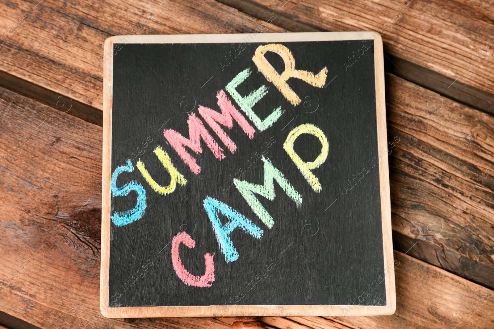 Photo of Little blackboard with text SUMMER CAMP chalked in different colors on table, top view