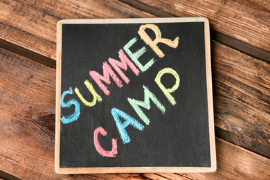 Photo of Little blackboard with text SUMMER CAMP chalked in different colors on table, top view