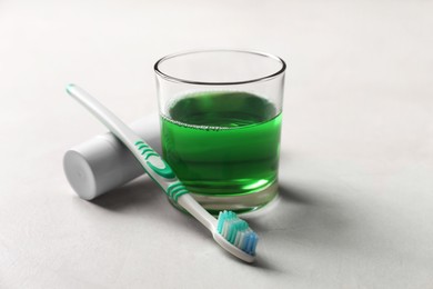 Fresh mouthwash in glass, toothpaste and toothbrush on light background, closeup