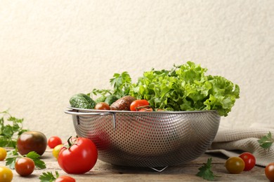 Wet vegetables in colander on wooden table, closeup