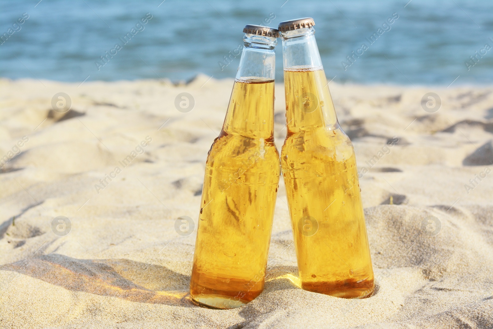 Photo of Bottles of cold beer on sandy beach near sea