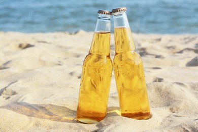 Bottles of cold beer on sandy beach near sea
