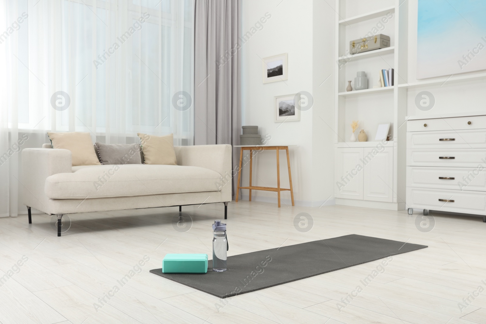 Photo of Exercise mat, yoga block and bottle of water on floor in room