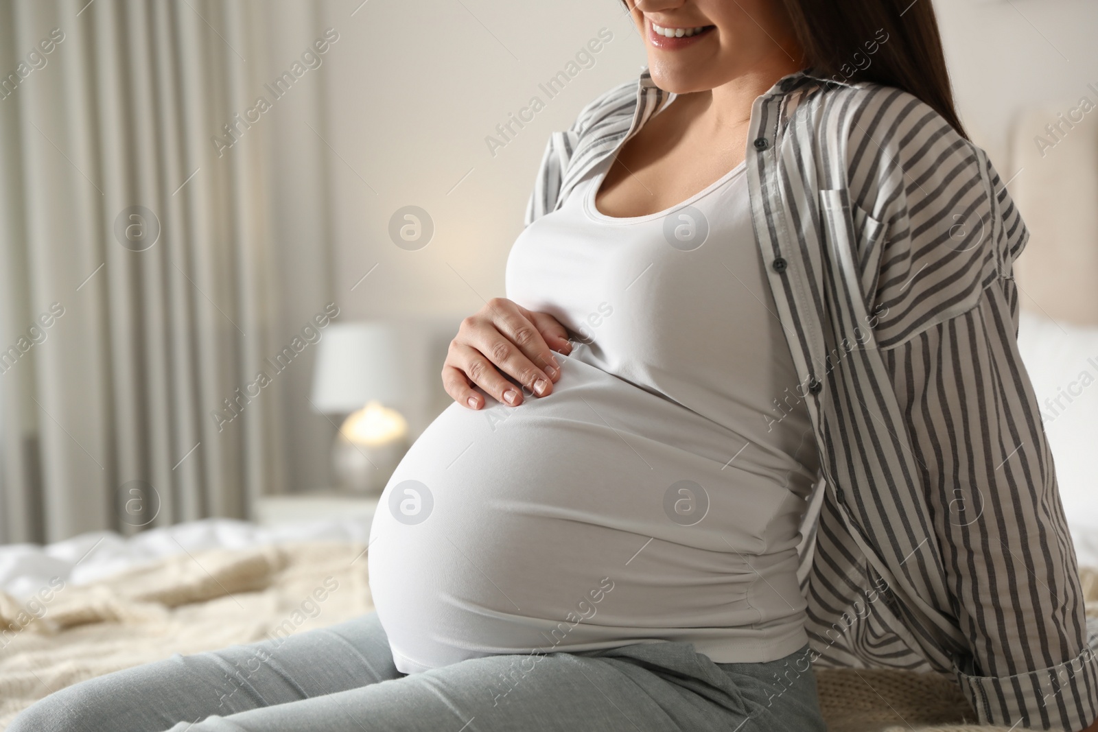 Photo of Young pregnant woman sitting on bed at home, closeup