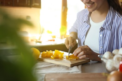 Photo of Woman cutting yellow bell peppers at countertop in kitchen, closeup. Space for text