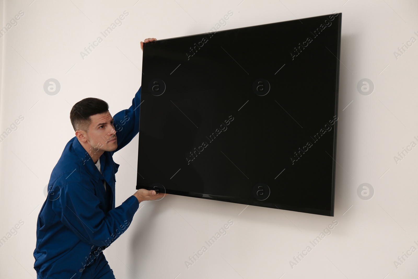 Photo of Professional technician installing modern flat screen TV on wall indoors