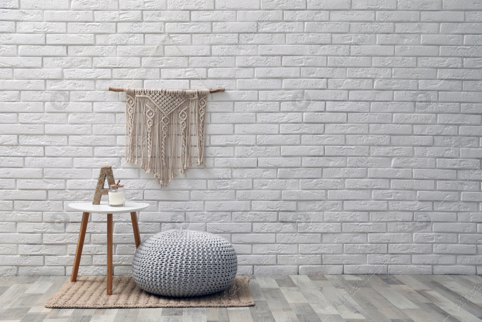 Photo of Comfortable knitted pouf, table and decor elements near white brick wall indoors, space for text. Interior design