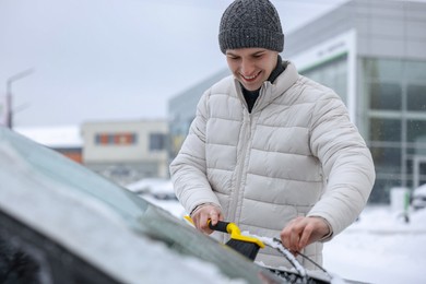 Photo of Man cleaning snow from car windshield outdoors, space for text