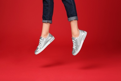 Woman in stylish sport shoes jumping on color background