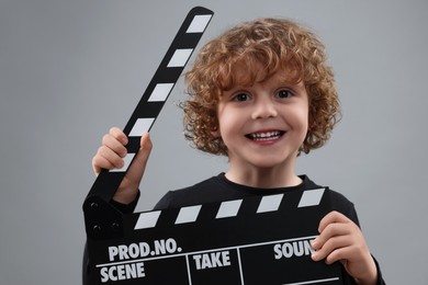Photo of Smiling cute boy with clapperboard on grey background. Little actor