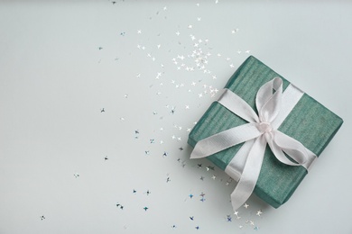 Photo of Blue gift box and shiny confetti on light background, top view. Space for text