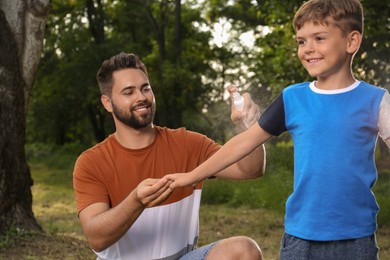 Man applying insect repellent on his son's arm in park. Tick bites prevention