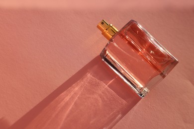 Luxury women's perfume. Sunlit glass bottle on pale pink background, top view. Space for text