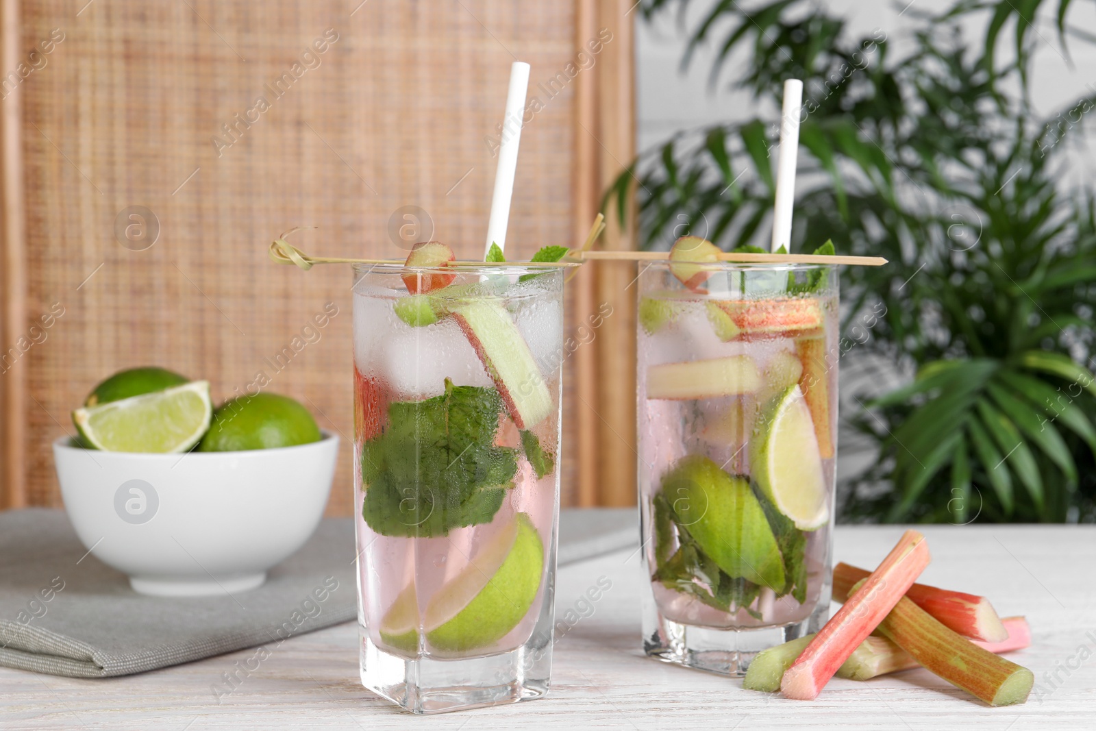 Photo of Tasty rhubarb cocktail with lime on white wooden table indoors