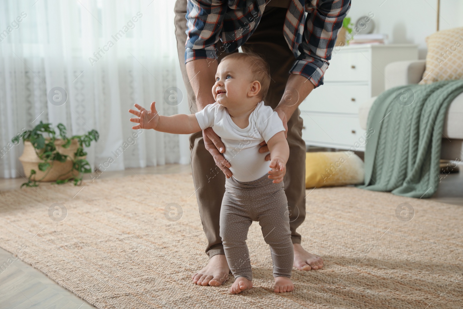 Photo of Father supporting his baby daughter while she learning to walk at home