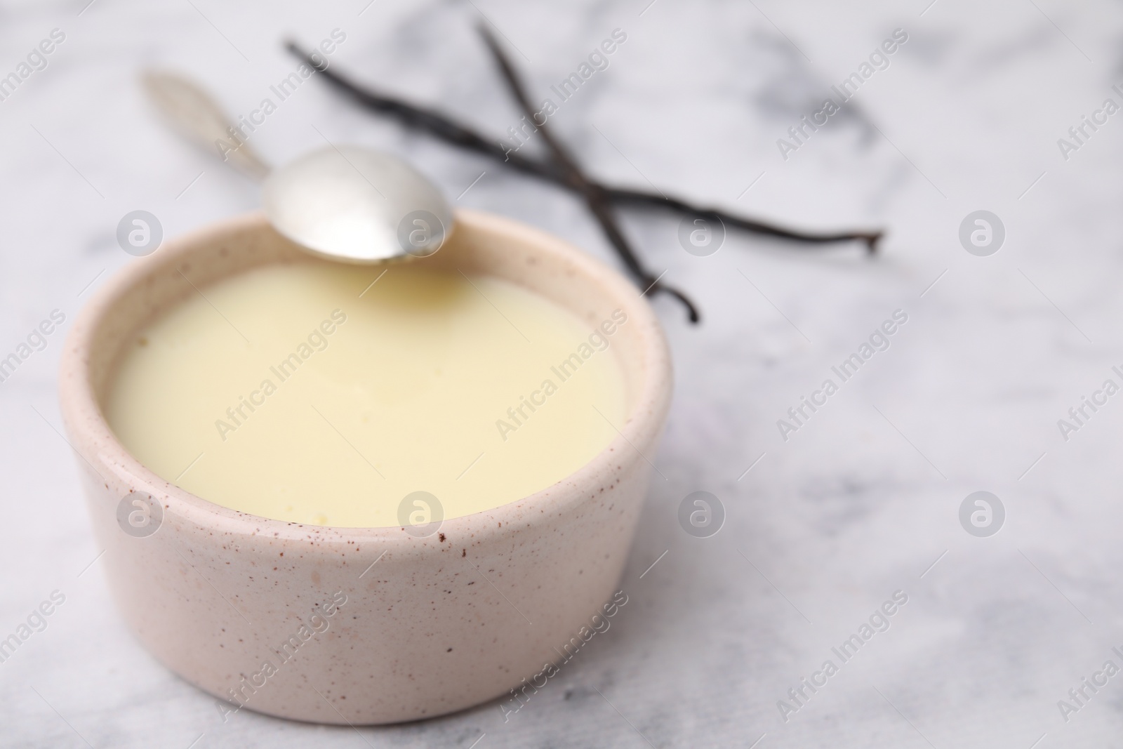 Photo of Bowl with condensed milk, vanilla pods and spoon on white marble table, closeup. Space for text