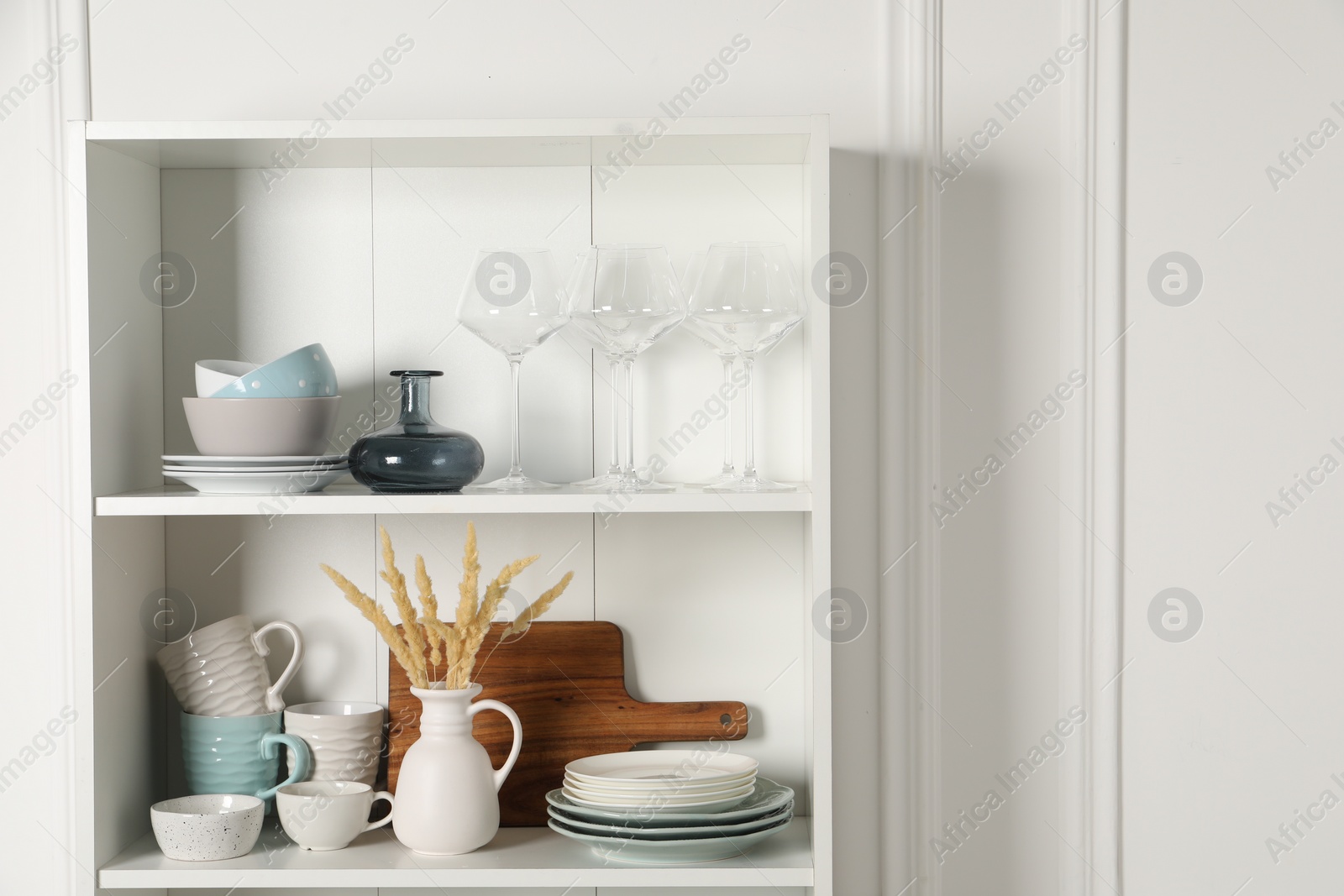 Photo of Different ceramic dishware and glasses on shelves in cabinet indoors. Space for text