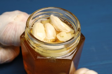 Photo of Honey with garlic in glass jar on blue wooden table, closeup