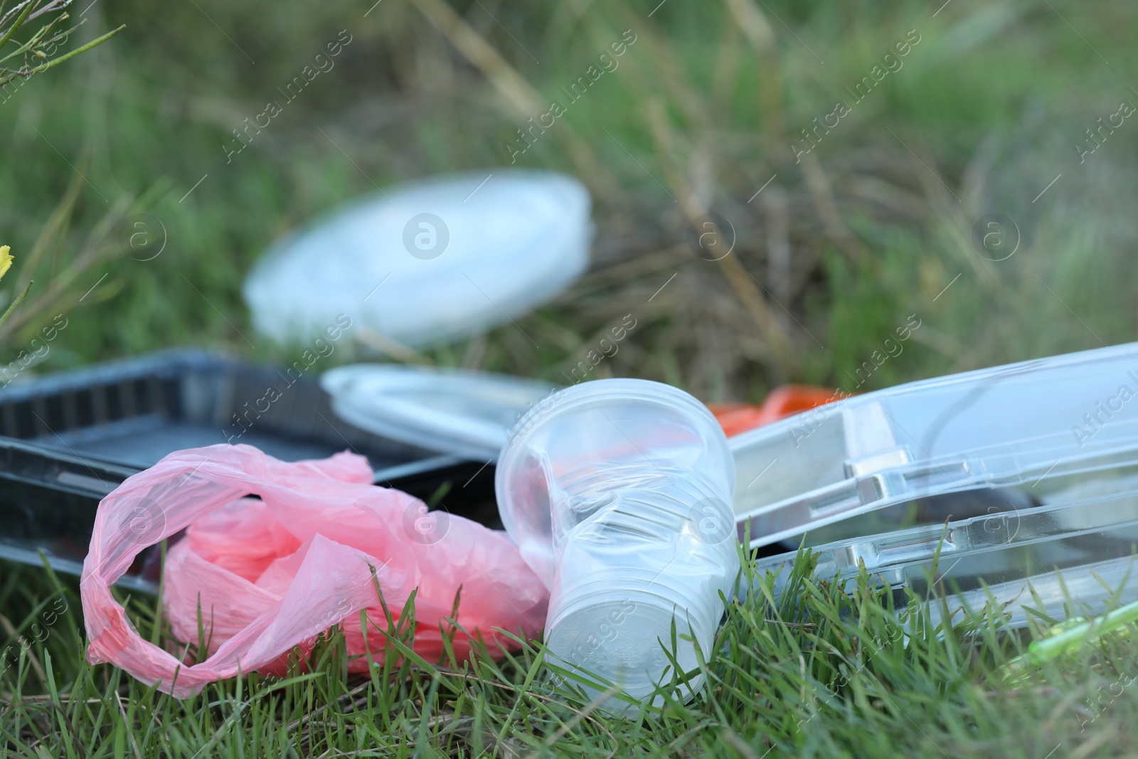 Photo of Used plastic tableware and bag on grass outdoors, closeup and space for text. Environmental pollution concept