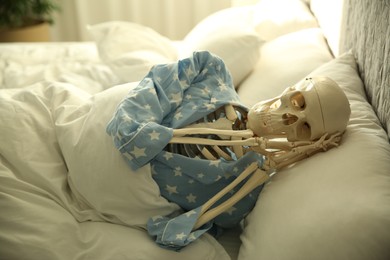 Photo of Human skeleton in pajamas lying on bed indoors