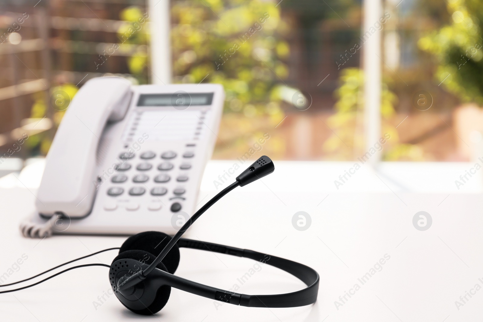 Photo of Headset and desk phone on table, space for text. Technical support concept