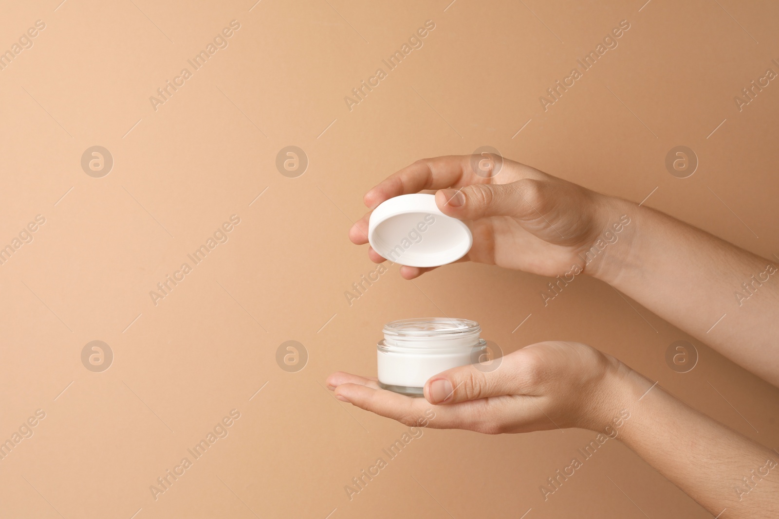 Photo of Woman holding jar of face cream on beige background, closeup. Space for text